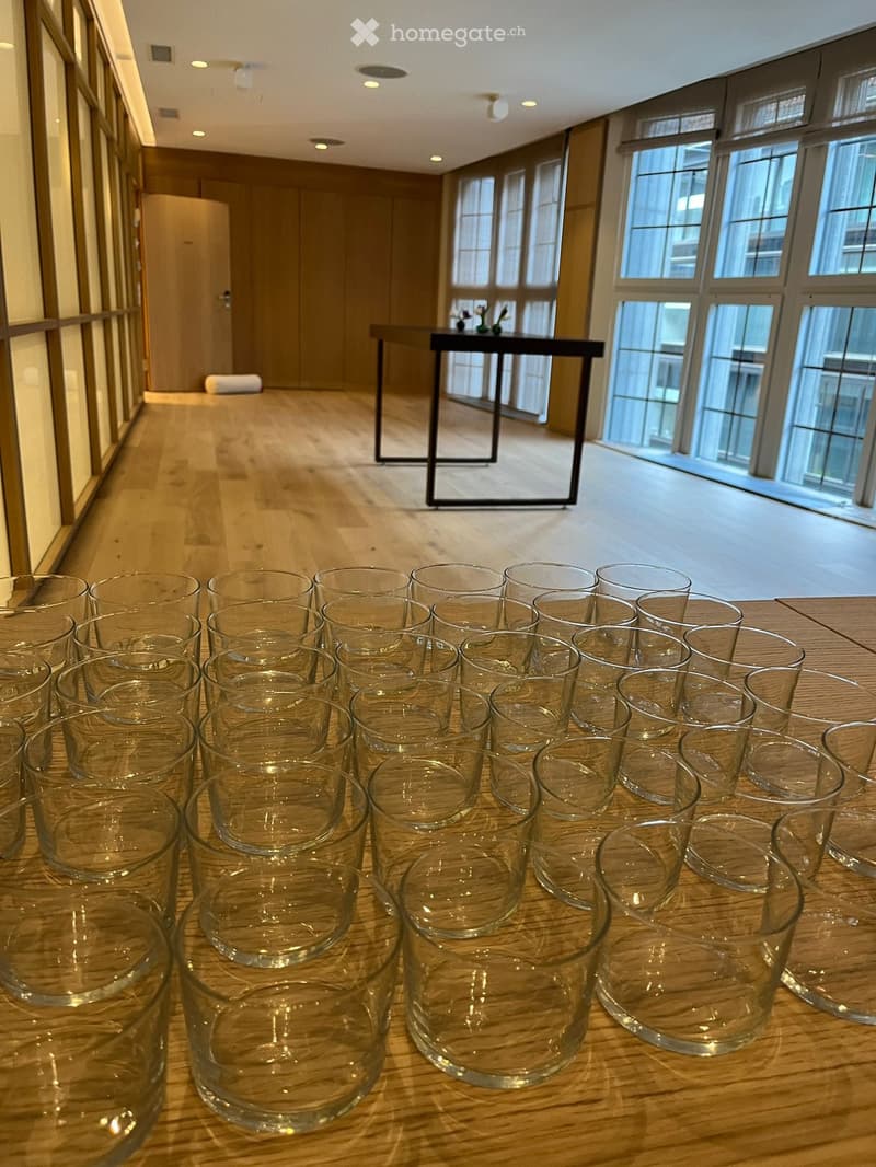 Empty room with wooden floor, large windows, a table with flowers, and a row of glasses on a table