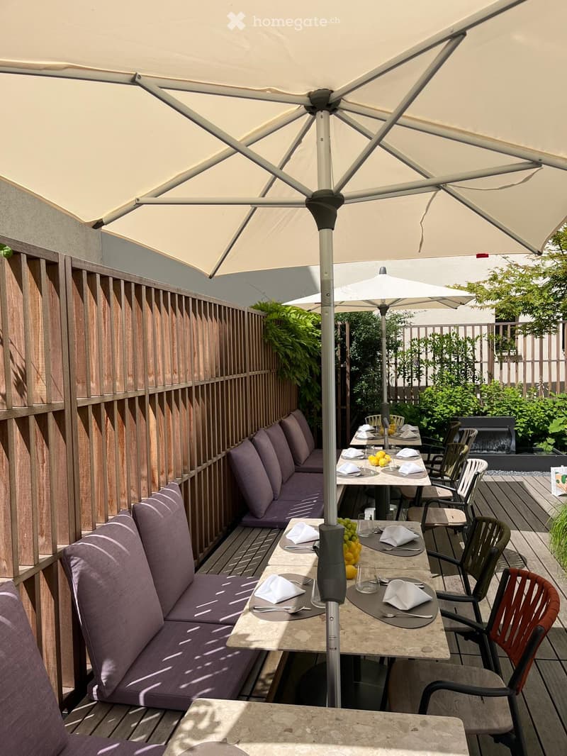 Outdoor seating area with tables, chairs, and umbrellas, wooden benches, and a wooden fence