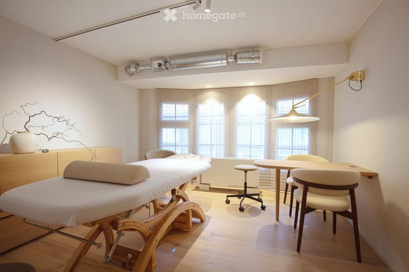 massage table, wooden floor, white walls, windows, wooden desk, chairs, lamp