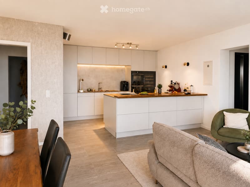 Modern open-plan living and kitchen area with white cabinets, a central island, a sofa, a dining table, and various kitchen appliances.