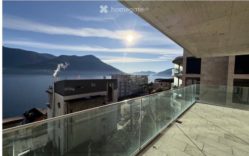Balcony with glass railing, overlooking a lake and mountains, sunny day.