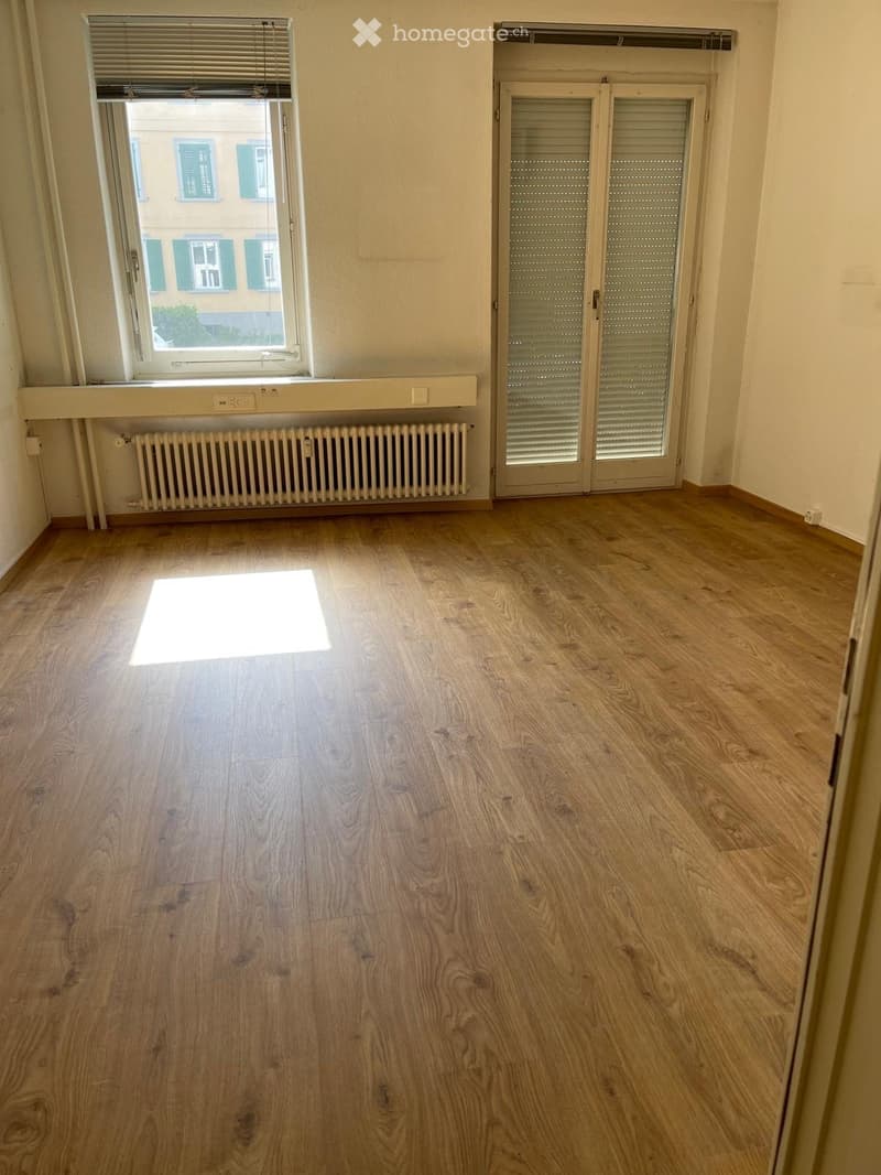 Empty room with wooden flooring, a window with blinds, a radiator, and a closed door with blinds.