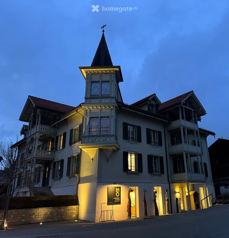 A multi-story residential building with a distinctive tower and illuminated windows, featuring balconies and decorative railings.
