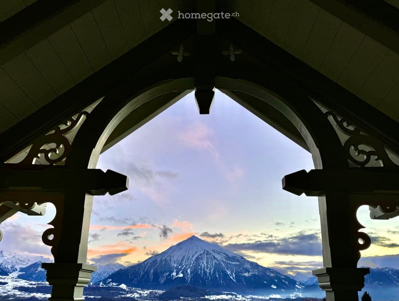 Balcony with ornate wooden railings, overlooking a snow-capped mountain range at sunset.