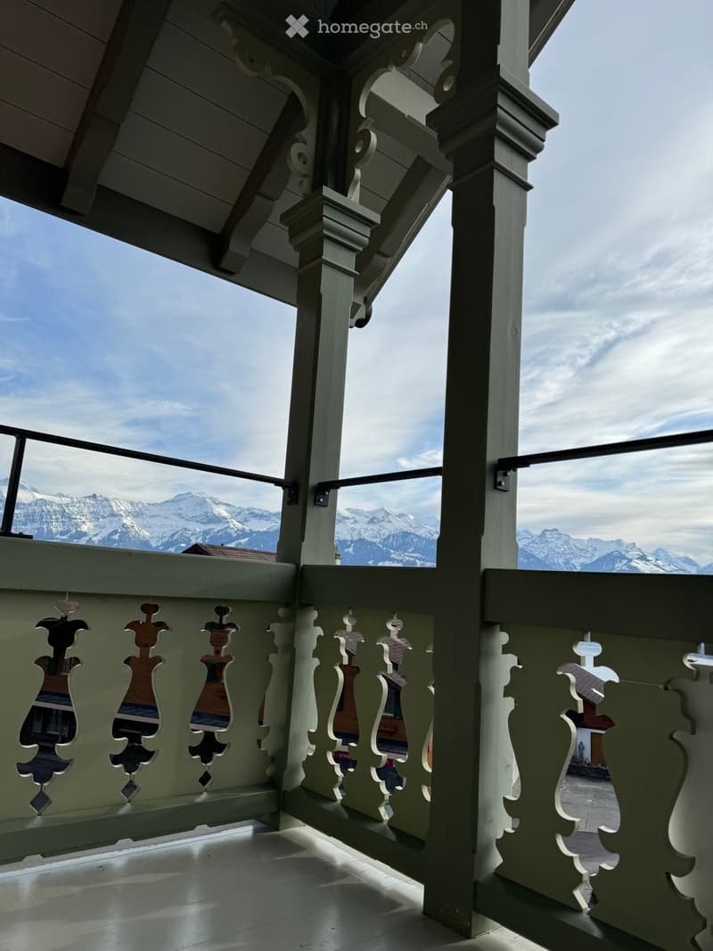 Balcony with ornate wooden railings and a view of snow-capped mountains.