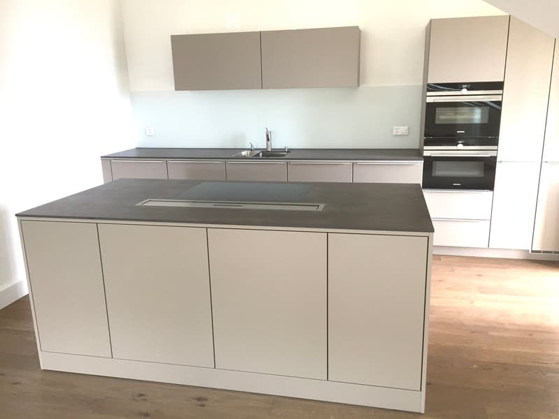 Modern kitchen with a central island, built-in oven, sink, and light grey cabinets.