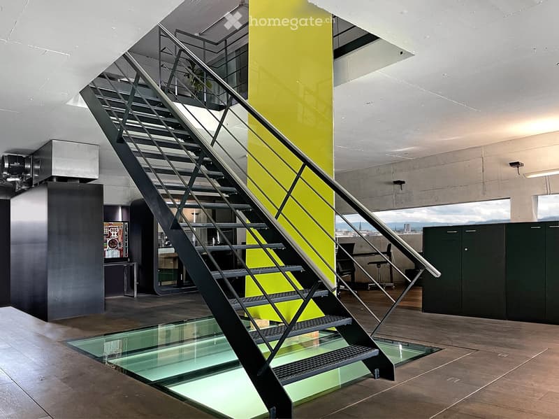 Modern interior with a sleek staircase featuring glass steps and metal railings, leading to an upper level. The space includes a bright yellow accent wall, contemporary furniture, and a view of a cityscape through large windows.