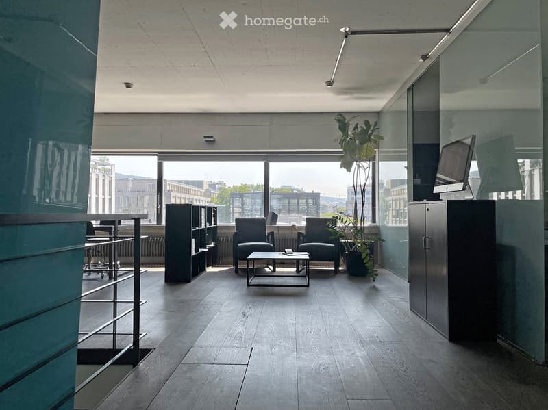 Modern, minimalist room with large windows, wooden floor, sofa, coffee table, chairs, screen, and plants.