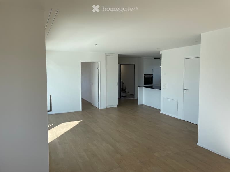 Empty room with light wooden flooring and white walls, featuring several doorways leading to other spaces.