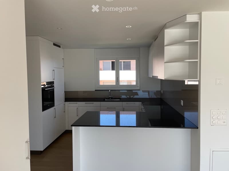 Modern kitchen with white cabinets, black countertops, and a central island. Features include an oven, sink, and faucet.