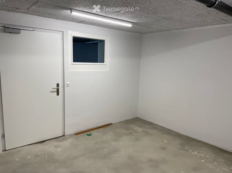 Empty room with white walls, concrete floor, a single window, and a white door. No furniture or equipment present.