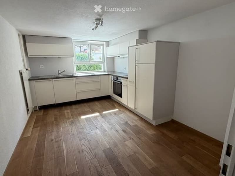 Modern kitchen with light grey cabinets, wooden flooring, and built-in appliances including a sink, oven, and refrigerator.
