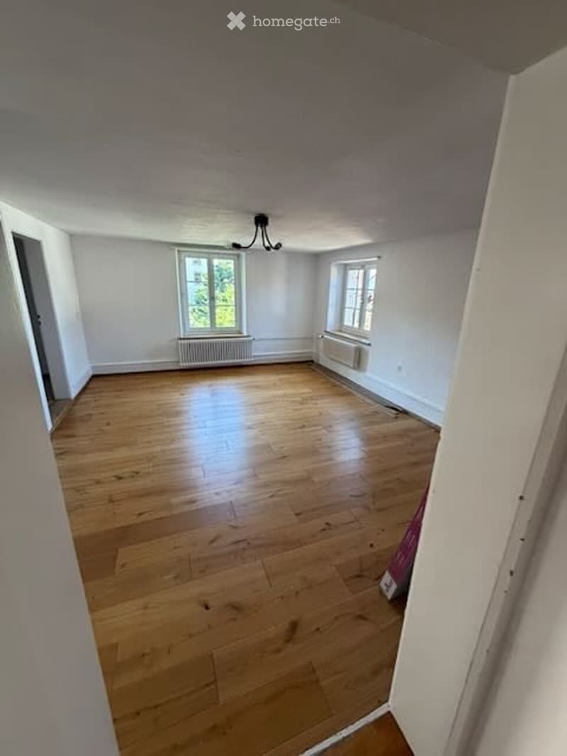 Empty room with wooden flooring, white walls, and two windows with radiators underneath. No furniture or equipment present.