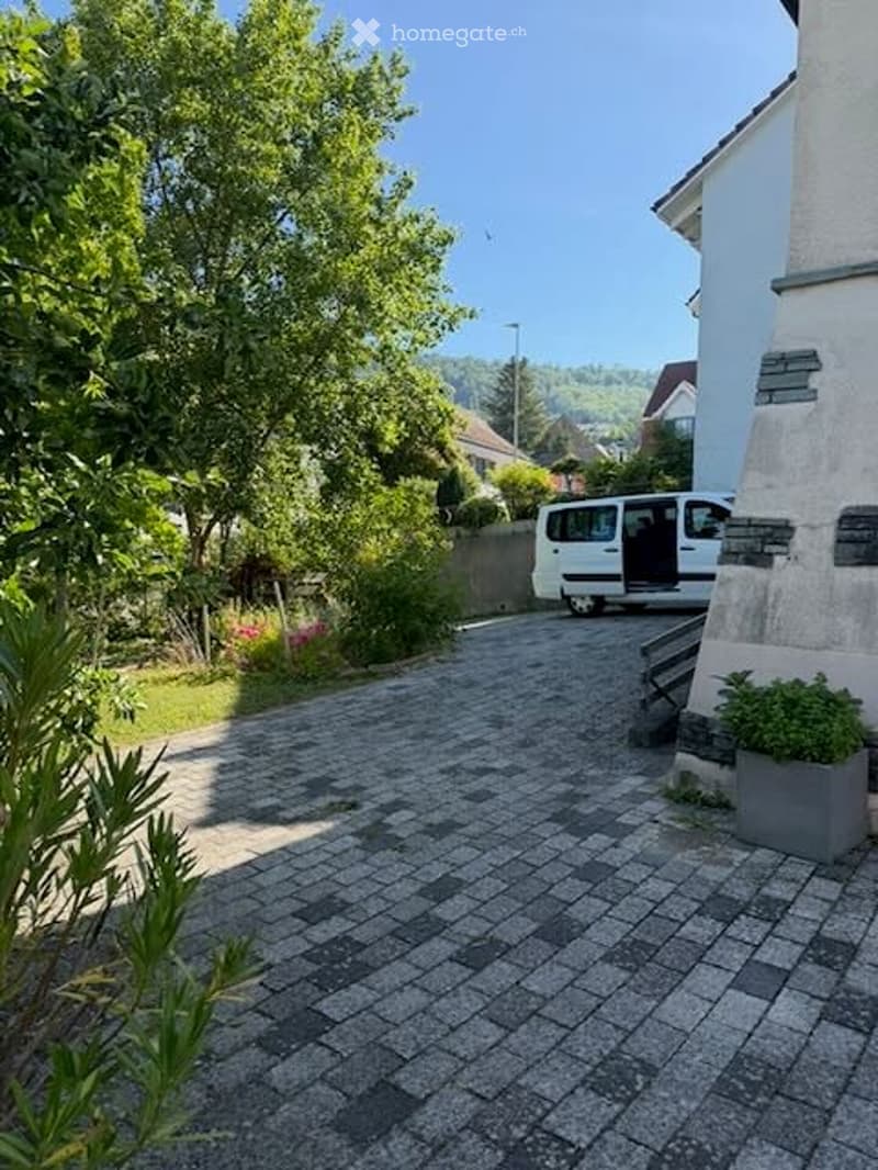 Driveway leading to a house with a parked van, surrounded by greenery and trees.