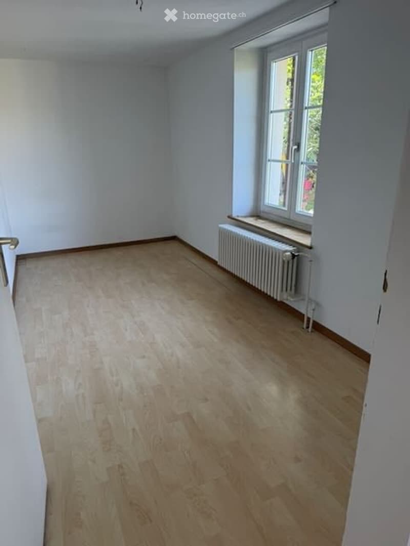 Empty room with light wooden flooring, white walls, and a single window with a radiator below it. No furniture or equipment present.