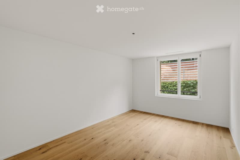 Empty room with white walls and light wooden flooring, featuring a single window with white frame and blinds.
