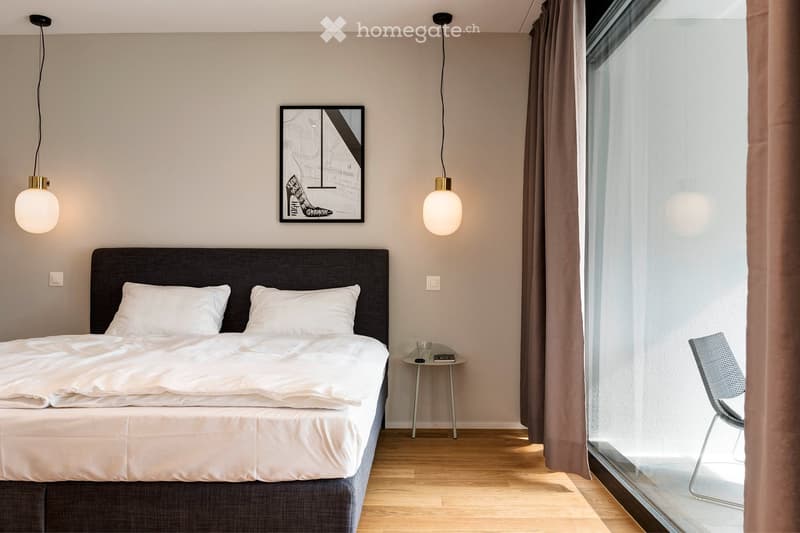 Modern bedroom with a large bed, nightstand, chair, pendant lights, and a picture frame on the wall.