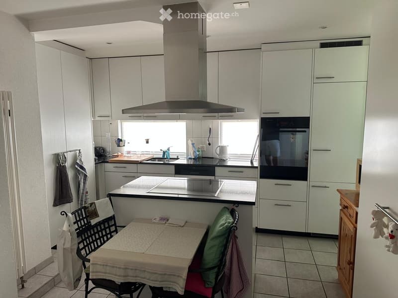 Modern kitchen with white cabinets, stainless steel appliances, a central island, and a small dining area with a table and chairs.