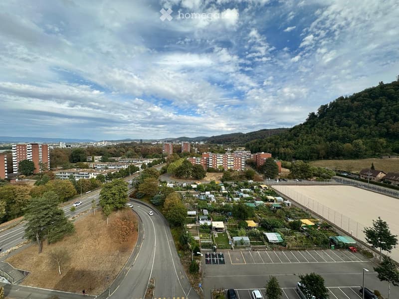 Aerial view of a residential area with apartment buildings, parking lots, a fenced sports field, and a garden area with small plots and greenhouses.