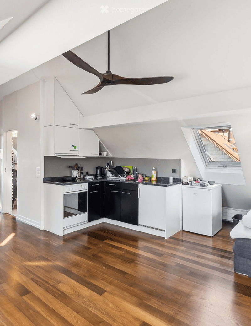 Modern kitchen with white cabinets, black countertops, and wooden flooring. Features include an oven, refrigerator, sink, and various kitchen appliances.
