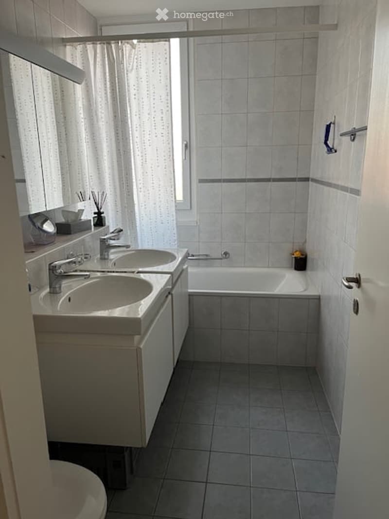 Modern bathroom with double sink vanity, bathtub, and tiled walls.