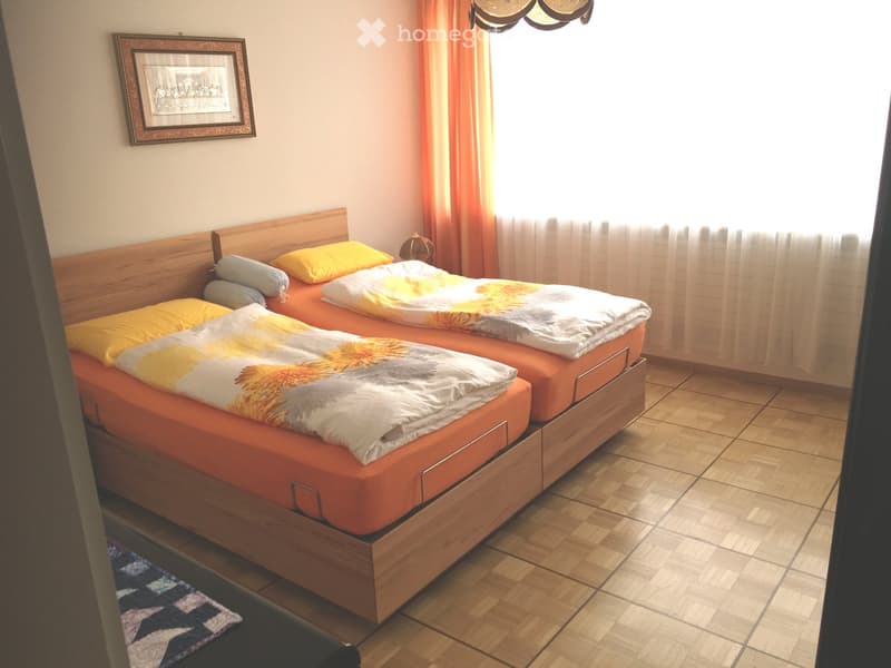 Cozy bedroom with two single beds, orange bedspreads, yellow and white pillows, wooden nightstand, lamp, and a framed picture on the wall.