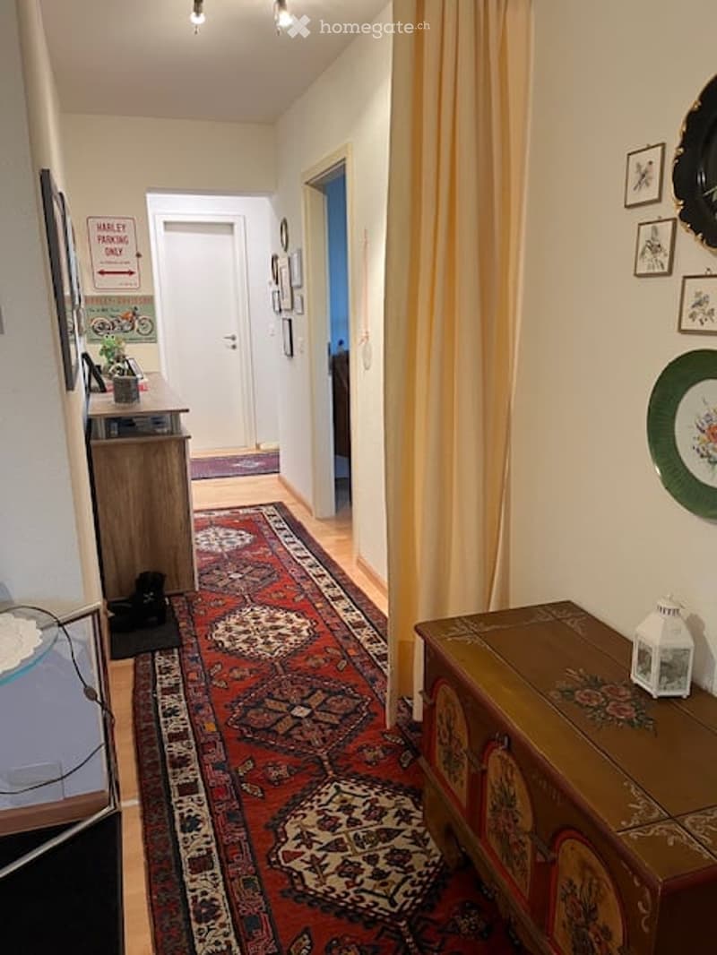 A hallway with carpet, wooden chest, framed art on wall, table with plant and sign, and yellow curtain