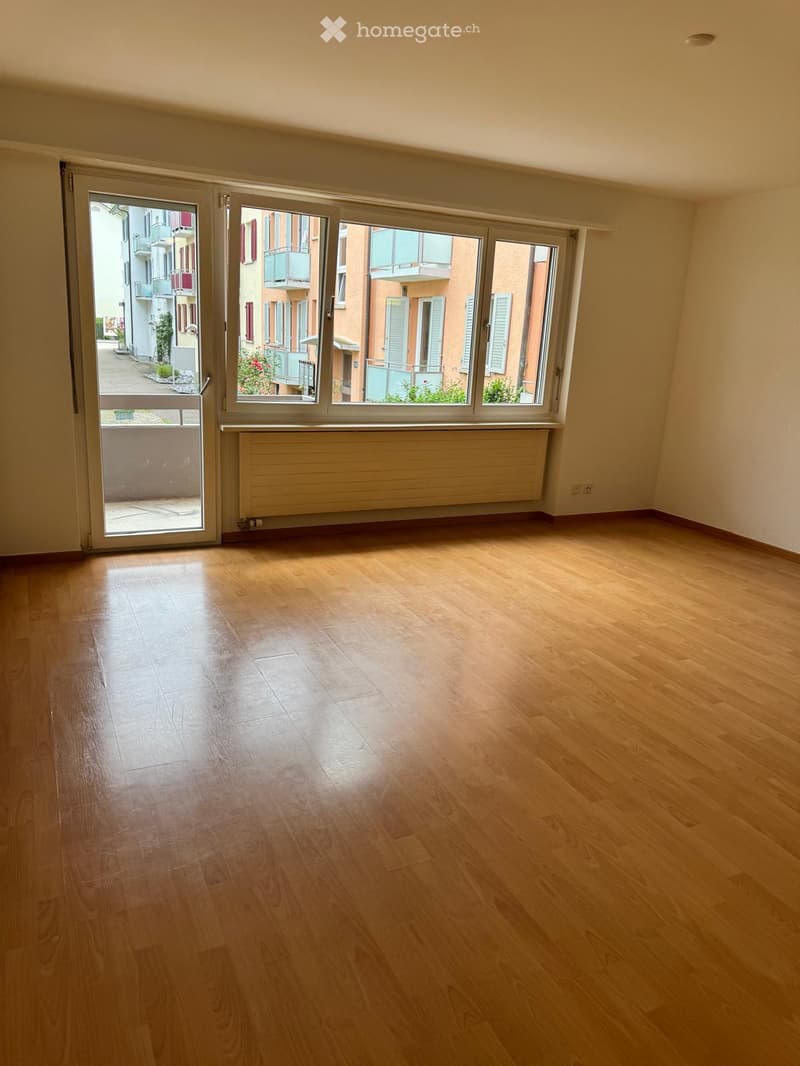 Empty room with wooden flooring, large windows, and a sliding glass door leading to a balcony.