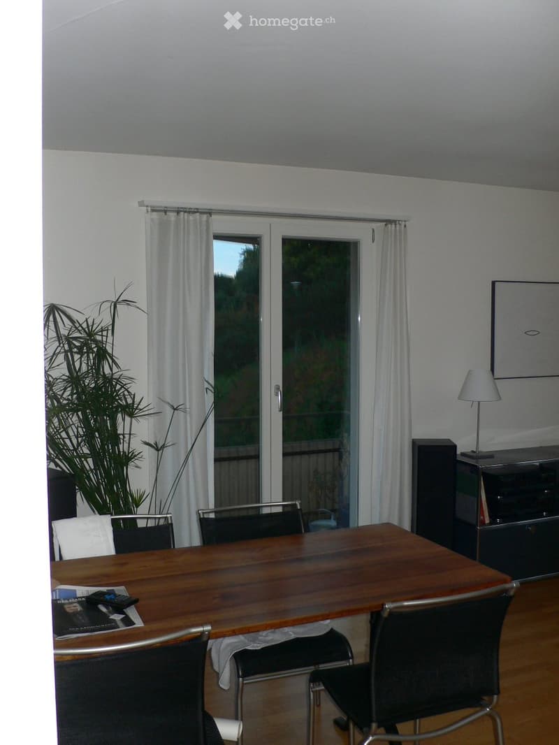 Dining area with wooden table, chairs, lamp, and large sliding glass door leading to a balcony.