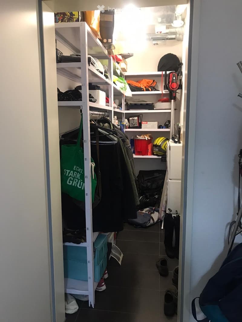 Well-lit closet with multiple shelves and hanging space, containing various items such as clothing, helmets, bags, and storage boxes.