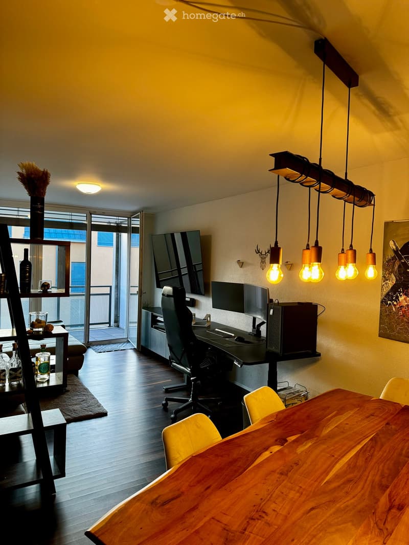 Modern living room with a large wooden table, chairs, a desk with a computer, and a balcony view.