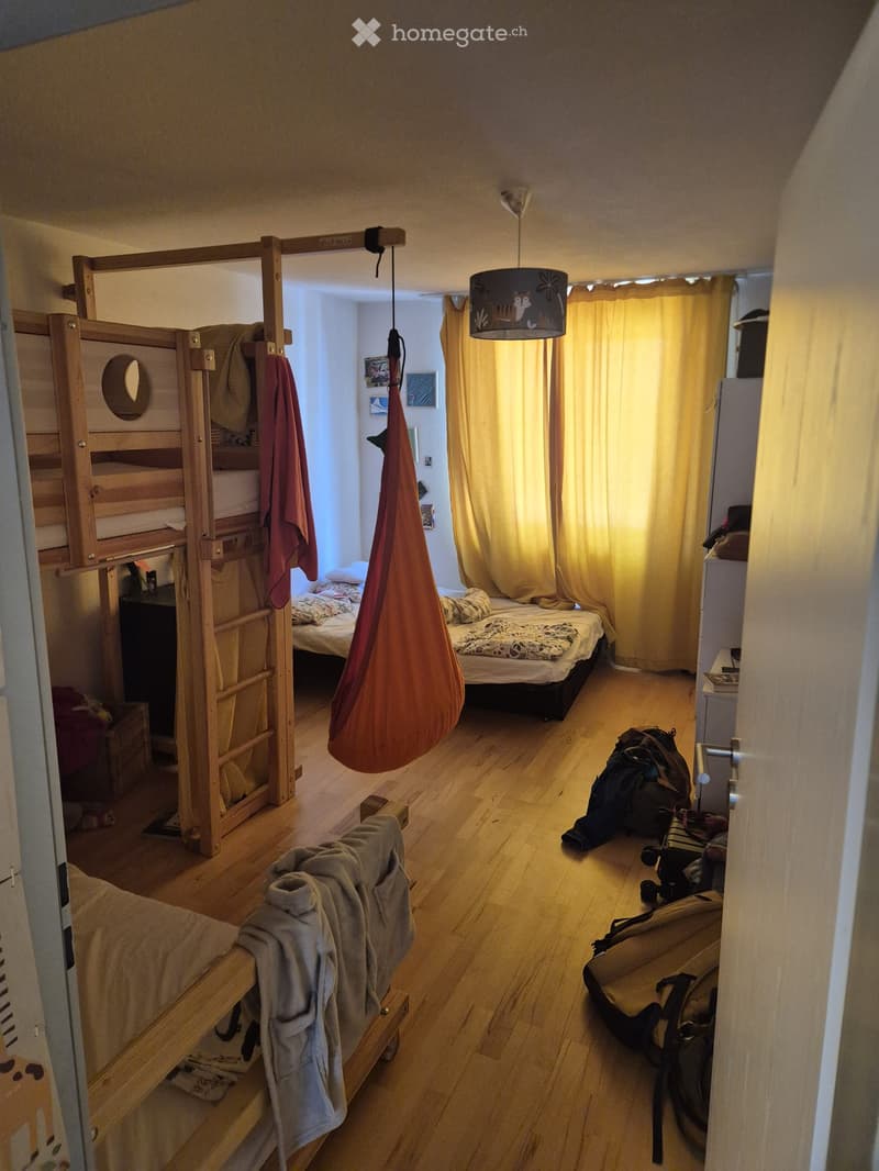 A small, cozy bedroom with a bunk bed, a single bed, a hanging egg chair, and a backpack on the floor.