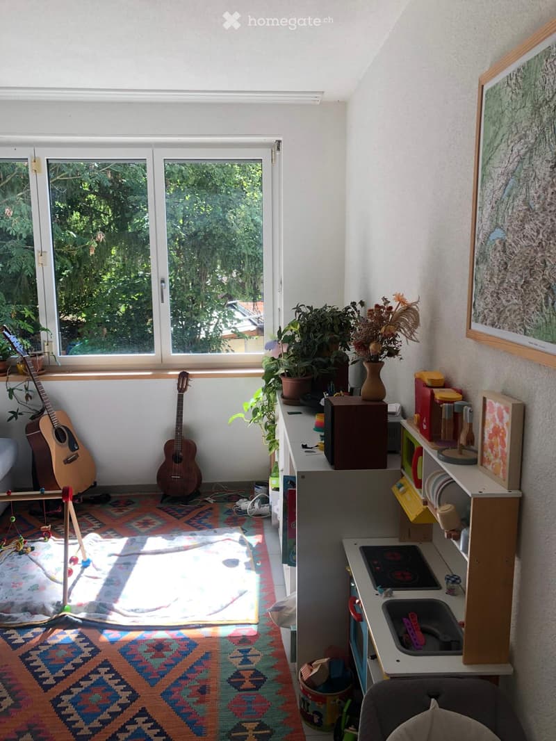 Bright room with large windows, kitchen area, guitars, plants, and toys.
