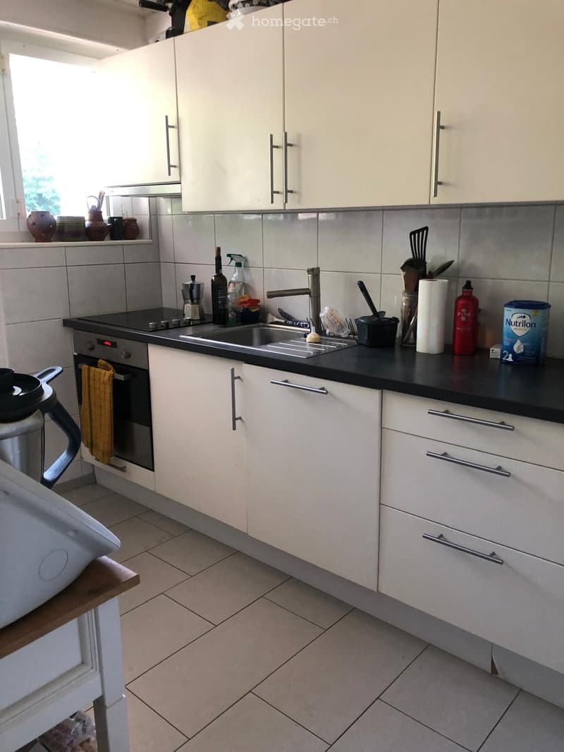 Modern kitchen with white cabinets, black countertops, stainless steel sink, and various kitchen items on the counter.