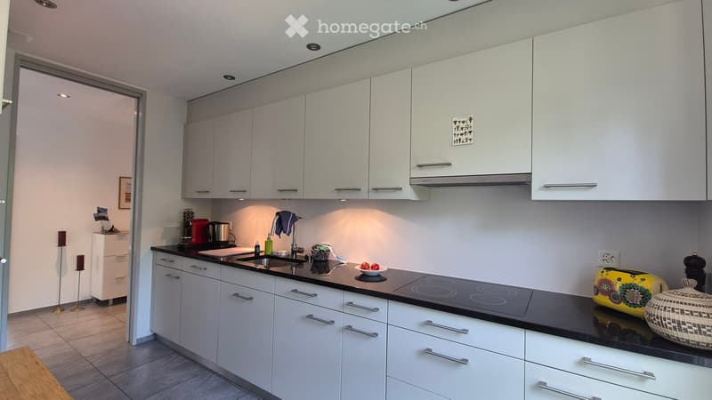 Modern kitchen with white cabinets, black countertops, induction cooktop, sink, and various appliances. Includes decorative items like candles and a vase on the counter.
