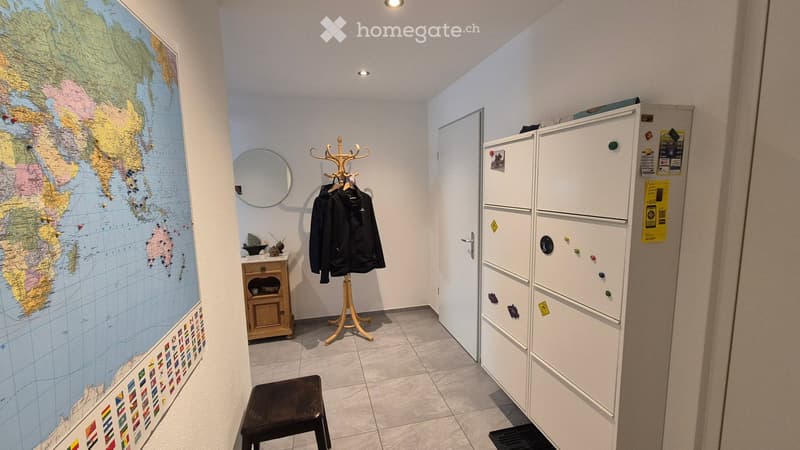 A small, well-lit hallway or entryway with a coat rack, a small wooden cabinet, a round mirror, a world map on the wall, and a stool.