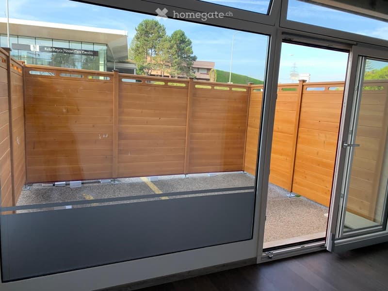 Balcony with wooden fence, sliding glass doors, and view of outdoor area with trees and buildings.