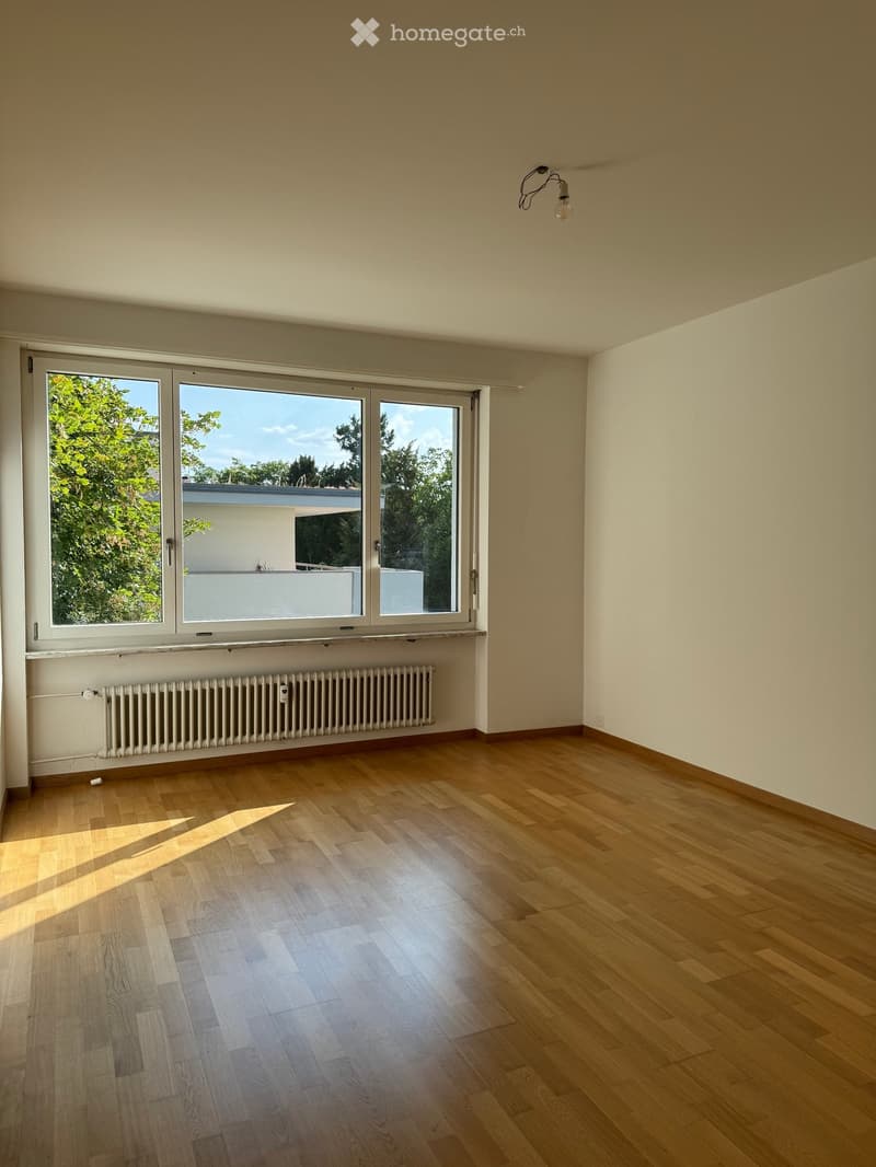 Empty room with wooden flooring, large windows, radiator, and a light fixture on the ceiling.