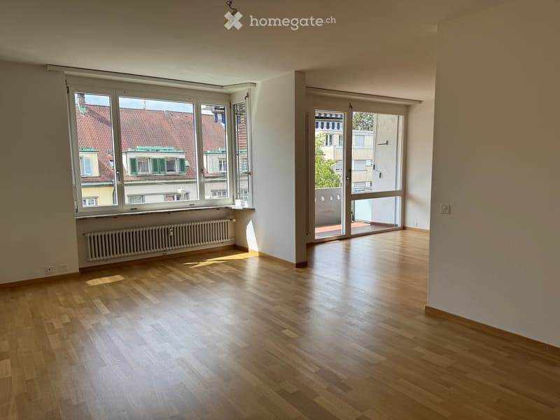 Empty room with wooden flooring, large windows, radiator, and sliding glass door leading to a balcony.