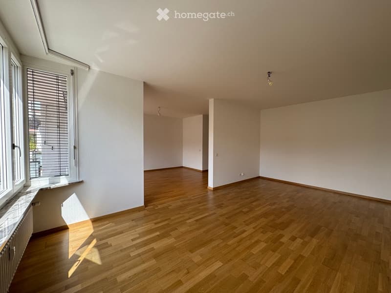 Empty room with wooden flooring, white walls, large windows with blinds, and a radiator. No furniture or equipment present.