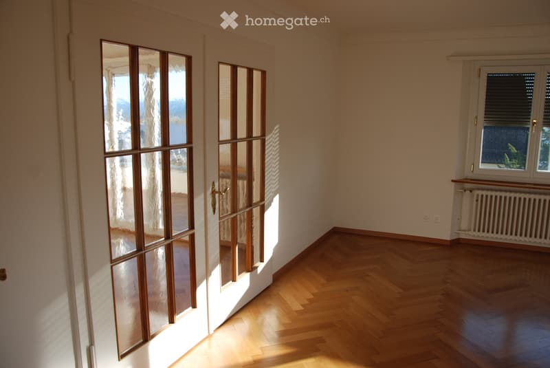 Empty room with wooden flooring, large glass doors leading outside, and a window with blinds.