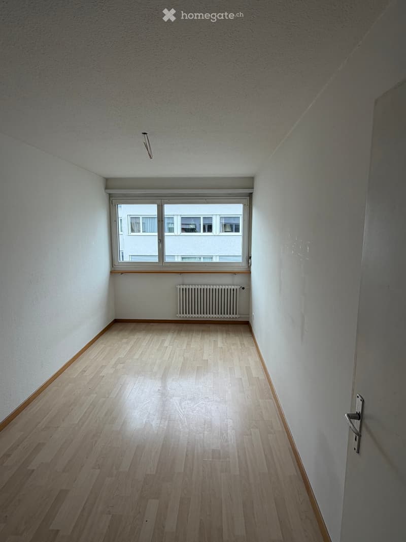 Empty room with light wooden flooring, white walls, and a large window with a radiator below it.