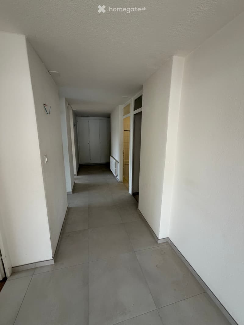 Empty hallway with tiled floor, white walls, and a closed door at the end.