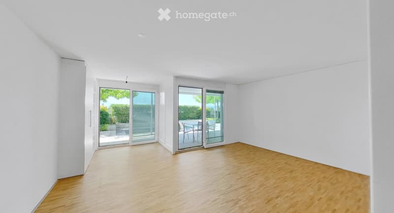 Empty room with white walls, wooden floor, and large glass sliding doors leading to an outdoor area.