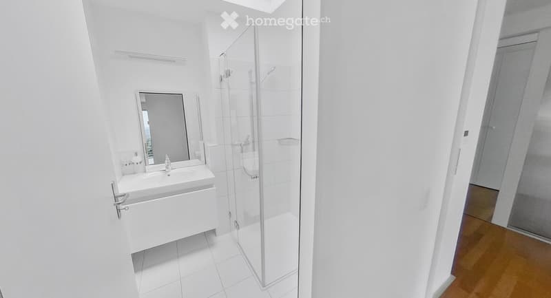 Modern bathroom with white tiles, a glass-enclosed shower, a white sink with a mirror, and a chrome faucet.