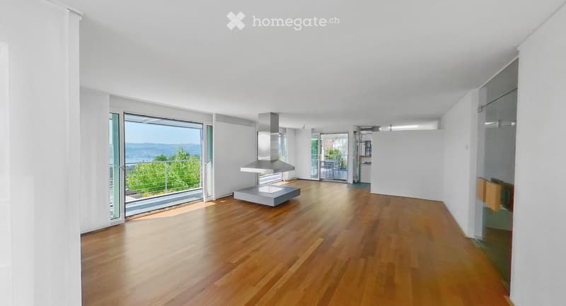 Bright, open living space with wooden flooring, large glass doors leading to a balcony with scenic views, a modern range hood, and a small table.