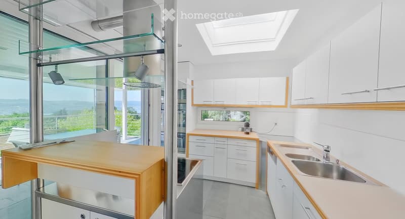 Modern kitchen with white cabinets, wooden countertops, a central island, and a large window offering a scenic view.