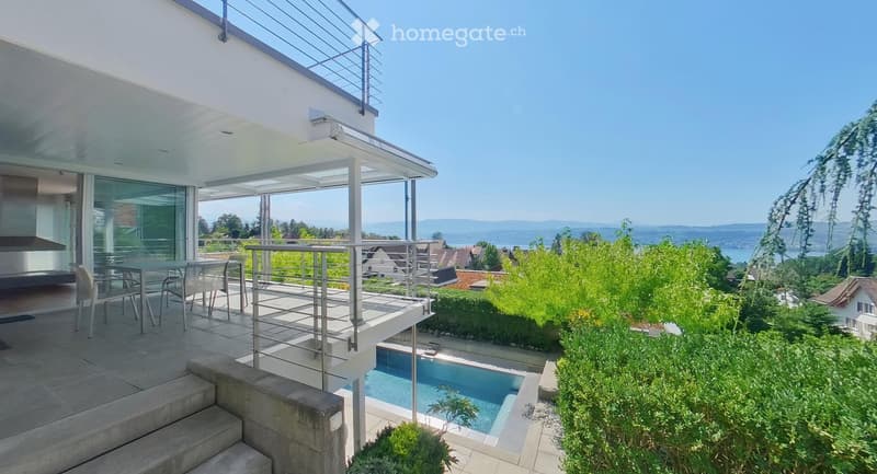 Modern outdoor area with a swimming pool, patio furniture, and scenic mountain view.