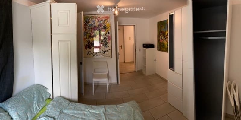 A furnished room with a bed, a chair, a cabinet, and a picture frame on the wall.