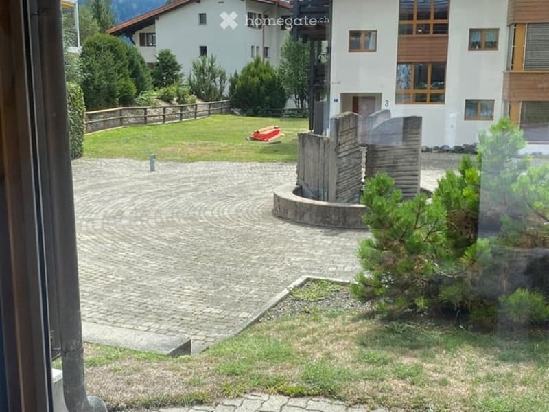 Courtyard with a circular brick pathway, small grassy areas, a wooden fence, and surrounding buildings.